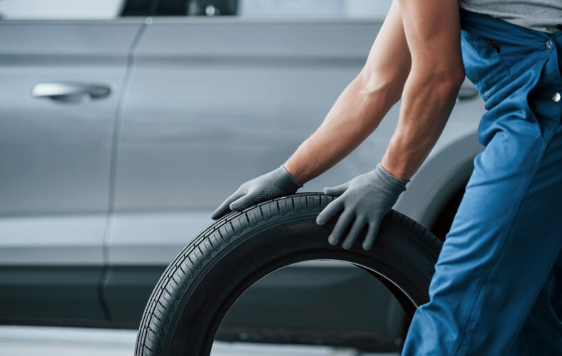 Art of transportation. Mechanic holding a tire at the repair garage. Replacement of winter and summer tires.