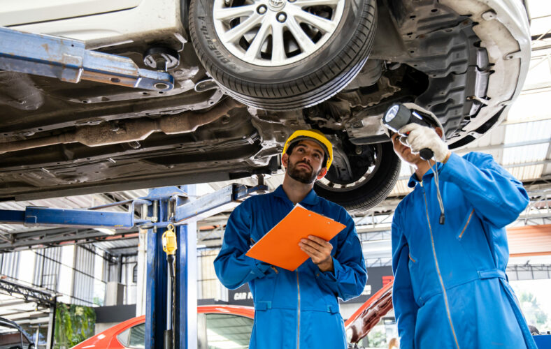 Two mechanic was checking the car suspension. Vehicle raised on lift at maintenance station. Car mechanic working at automotive service center.