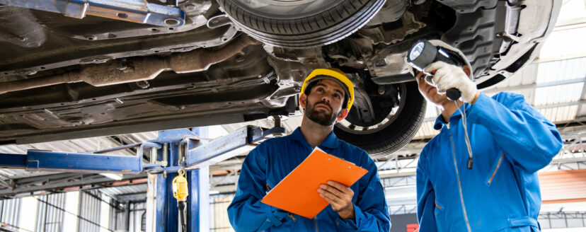 Two mechanic was checking the car suspension. Vehicle raised on lift at maintenance station. Car mechanic working at automotive service center.